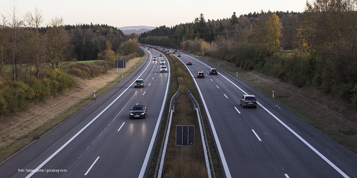 KI generiert: Das Bild zeigt eine Autobahn mit mehreren Autos, die in beide Richtungen fahren. Die Straße ist von Bäumen und leicht hügeliger Landschaft umgeben.