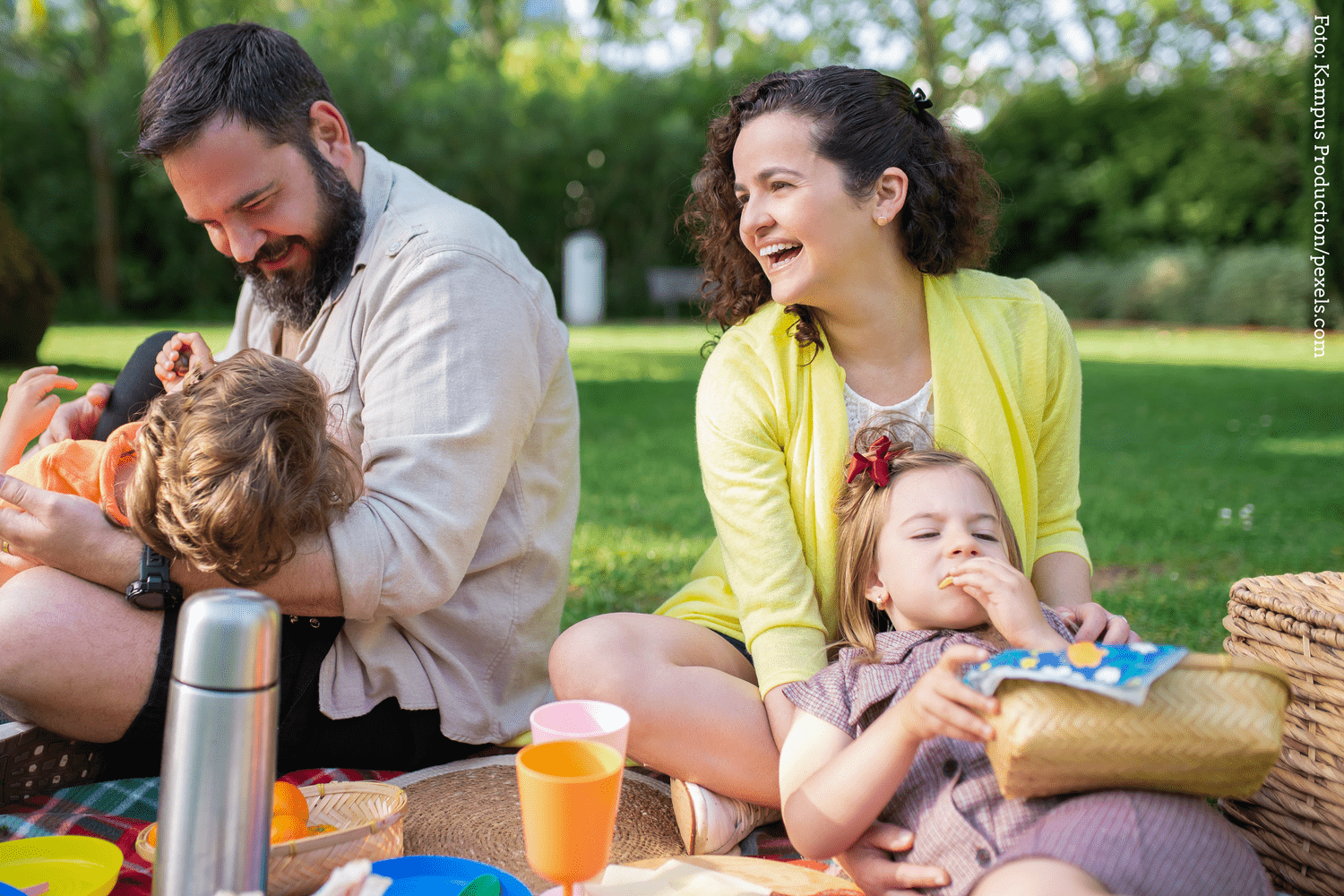 KI generiert: Eine Familie genießt bei gutem Wetter ein Picknick im Freien. Sie wirken fröhlich und entspannt, während sie zusammen auf einer Decke sitzen.