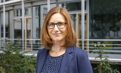 Aniela Liebezeit steht vor einer Gebäudestruktur und schaut in die Kamera.