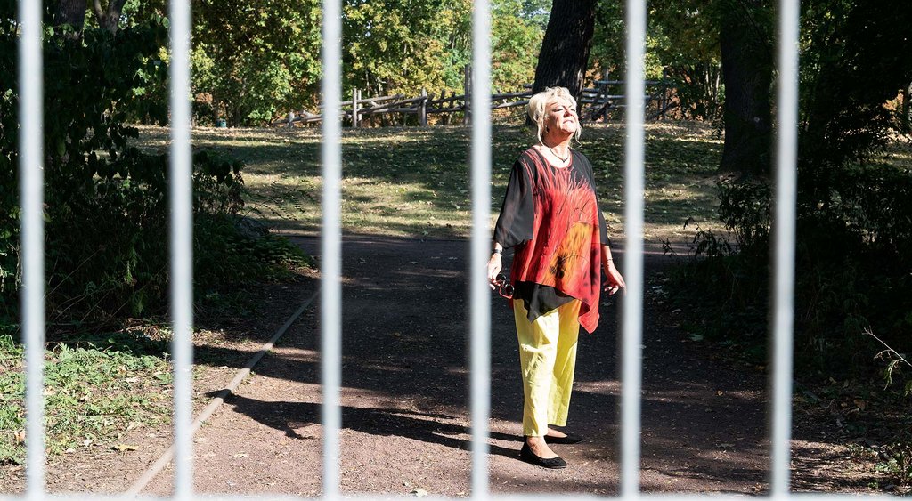Christina Staniok steht hinter einem Zaungitter in einem Park und steht mit geschlossenen Augen der Sonne zugewendet da.