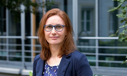 Aniela Liebezeit steht vor einer Gebäudestruktur und schaut in die Kamera.