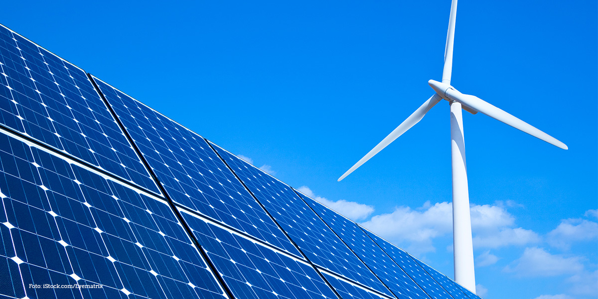 KI generiert: Das Bild zeigt Solarzellen im Vordergrund und eine Windkraftanlage im Hintergrund vor einem klaren blauen Himmel. Der Hauptinhalt des Bildes ist die Nutzung erneuerbarer Energien.