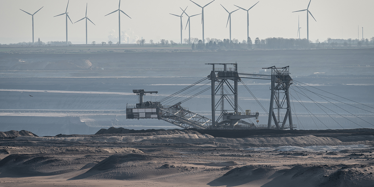 KI generiert: Das Bild zeigt einen Tagebau mit einem großen Schaufelradbagger im Vordergrund und Windkraftanlagen im Hintergrund. Es thematisiert den Gegensatz zwischen fossiler und erneuerbarer Energiegewinnung.