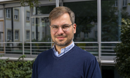 Markus Wulff steht vor einer Gebäudestruktur und schaut in die Kamera.