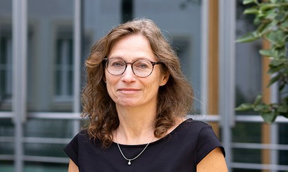 Andrea Jödecke steht vor einer Gebäudestruktur und schaut in die Kamera.