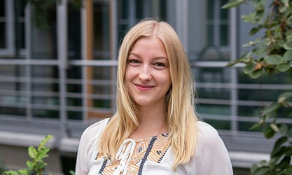 Caroline Jüling steht vor einer Gebäudestruktur und schaut in die Kamera.