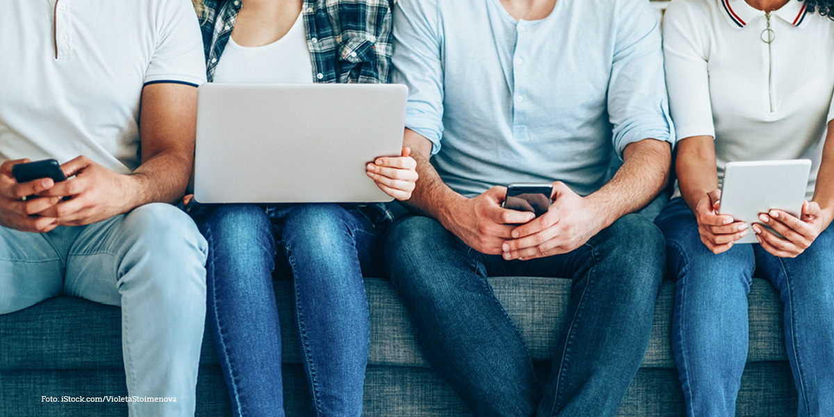 KI generiert: Das Bild zeigt vier Personen, die auf einer Couch sitzen und jeweils ein elektronisches Gerät wie Smartphone, Laptop oder Tablet in den Händen halten. Es illustriert die Nutzung von moderner Technologie im Alltag.