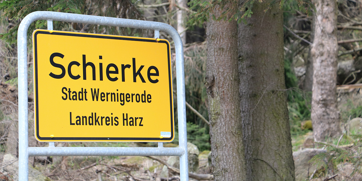 KI generiert: Das Bild zeigt ein Ortsschild mit der Aufschrift "Schierke" und enthält Informationen zur Stadt Wernigerode und dem Landkreis Harz. Im Hintergrund sind Bäume zu sehen.